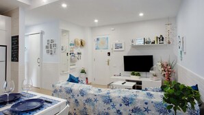 Una sala de estar moderna con un televisor de pantalla plana, una mesa de comedor con mantel azul y un sofá con funda estampada.