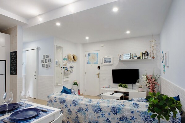 Una sala de estar moderna con un televisor de pantalla plana, una mesa de comedor con mantel azul y un sofá con funda estampada.