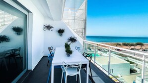 Un balcon avec une table et des chaises blanches, des plantes en pot et une vue sur l’océan.