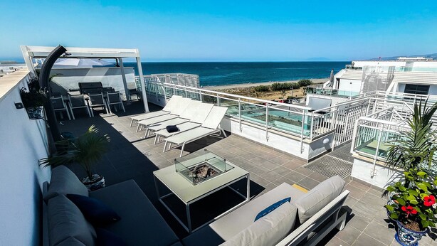 Une terrasse sur le toit avec des sièges extérieurs, une balustrade en verre et une vue sur l’océan.