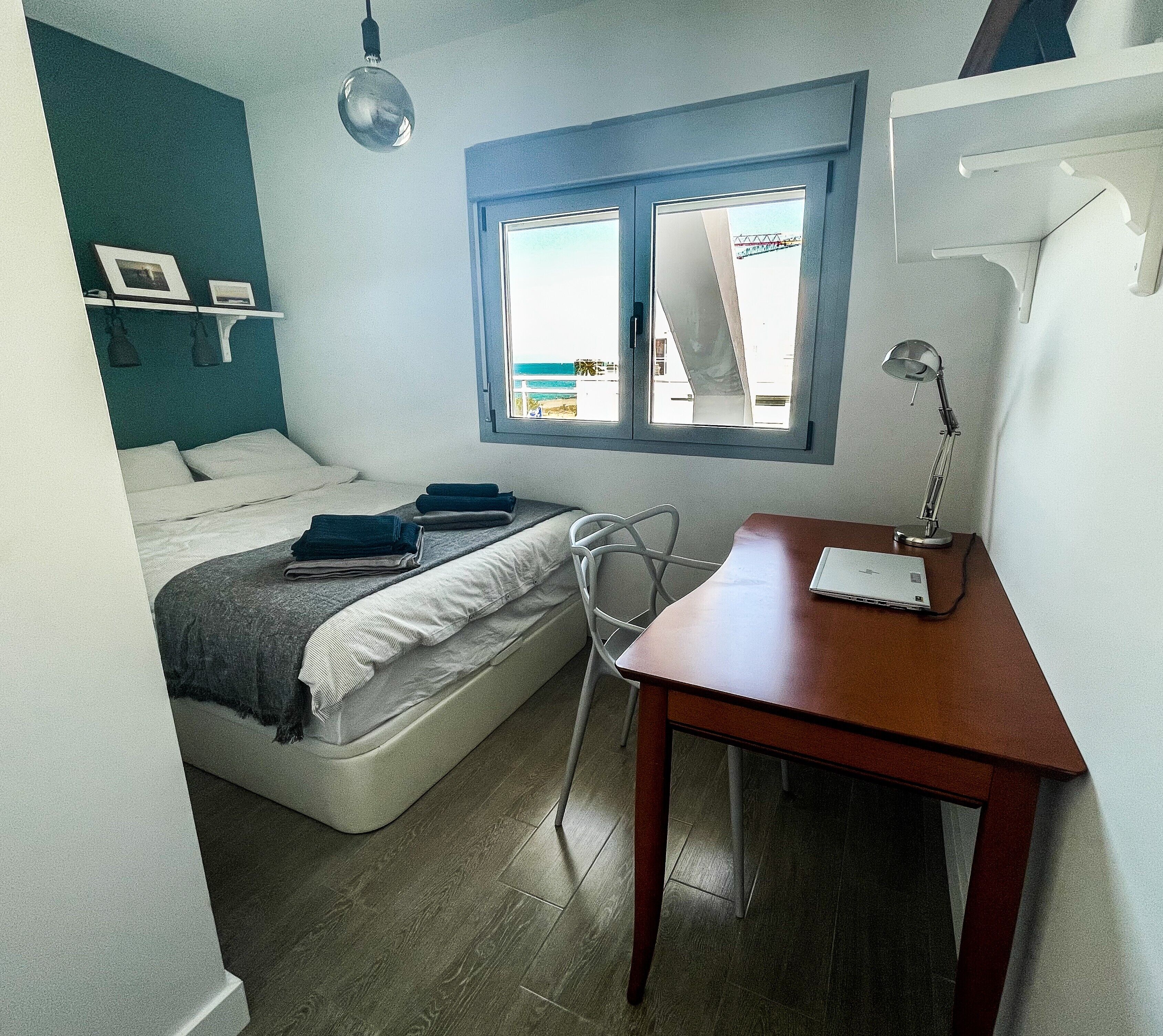 A compact room with a bed, a desk, a chair, a window, and a hanging light fixture.