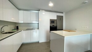 Une cuisine moderne avec des meubles blancs, un réfrigérateur en acier inoxydable, un four à micro-ondes et une planche à découper en bois posée sur l’îlot central.