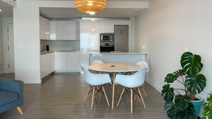 Une cuisine moderne avec des meubles blancs, un îlot central et un coin repas comprenant une table ronde et des chaises.