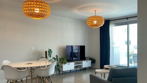 Un salon moderne comprenant un coin repas, un téléviseur à écran plat et deux lampes suspendues.