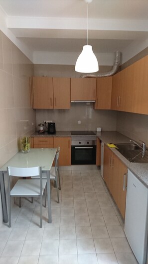 A compact kitchen with wooden cabinets, a stainless steel sink, a gas stove, and a hanging pendant light.