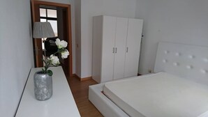 Ein Schlafzimmer mit einem Bett, einem Kleiderschrank, einer Lampe und einer Blumenvase.