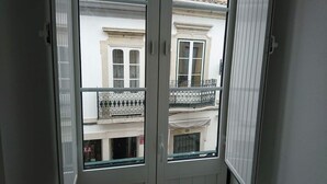 Blick durch ein Fenster mit Balkon, ein weißes Gebäude mit Fenster und Tür.