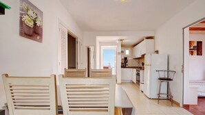 A dining area with wooden chairs and a bench, a kitchen in the background, and a door leading outside. - Apartment 'Beautiful 3-Bed' with Pool, Garden and Wi-Fi (Caleta De Fuste)