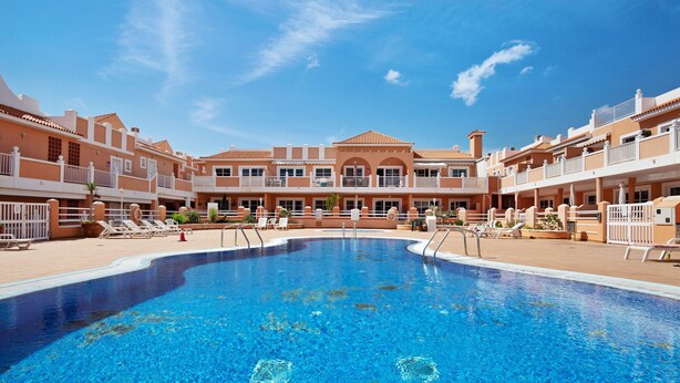 A swimming pool with lounge chairs and a building with balconies in the background. - Apartment 'Beautiful 3-Bed' with Pool, Garden and Wi-Fi (Caleta De Fuste)