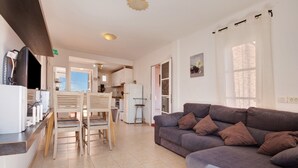 A modern living room with a grey sofa, wooden chairs, a kitchen area, and a dining table. - Apartment 'Beautiful 3-Bed' with Pool, Garden and Wi-Fi (Caleta De Fuste)
