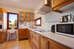 Une cuisine avec des meubles en bois, un plan de travail blanc, un four à micro-ondes et une fenêtre donnant sur un paysage verdoyant.