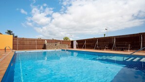 Une piscine avec une terrasse en bois, une clôture et un ciel dégagé.