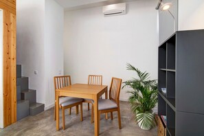 A dining area with a wooden table and chairs, a potted plant, a staircase, and a dark-colored bookshelf.