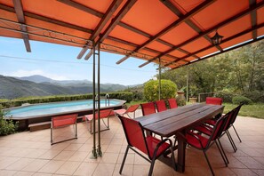 Un espacio al aire libre cubierto con piscina, sillas rojas y una mesa de madera.