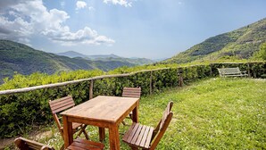A wooden table and chairs set outdoors with a view of green hills and a clear sky.