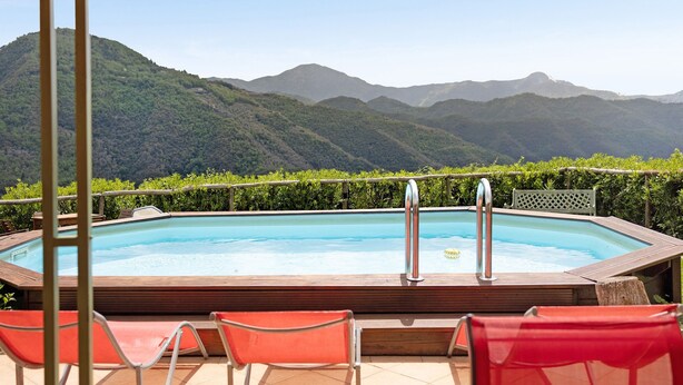 A rectangular pool with a wooden deck, surrounded by red chairs, and a view of green mountains in the background.