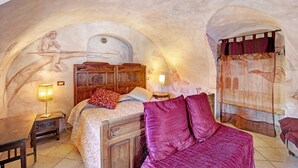 A bedroom with a bed, a wooden nightstand, a lamp, and a mural on the wall.