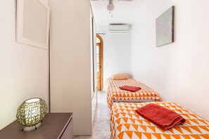 Ein Hotelzimmer mit zwei Betten, einer Wandklimaanlage und einer Tür zu einem weiteren Raum.