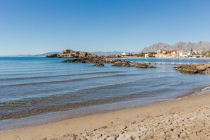 A beach with clear water, rocky outcrops, and distant mountains.