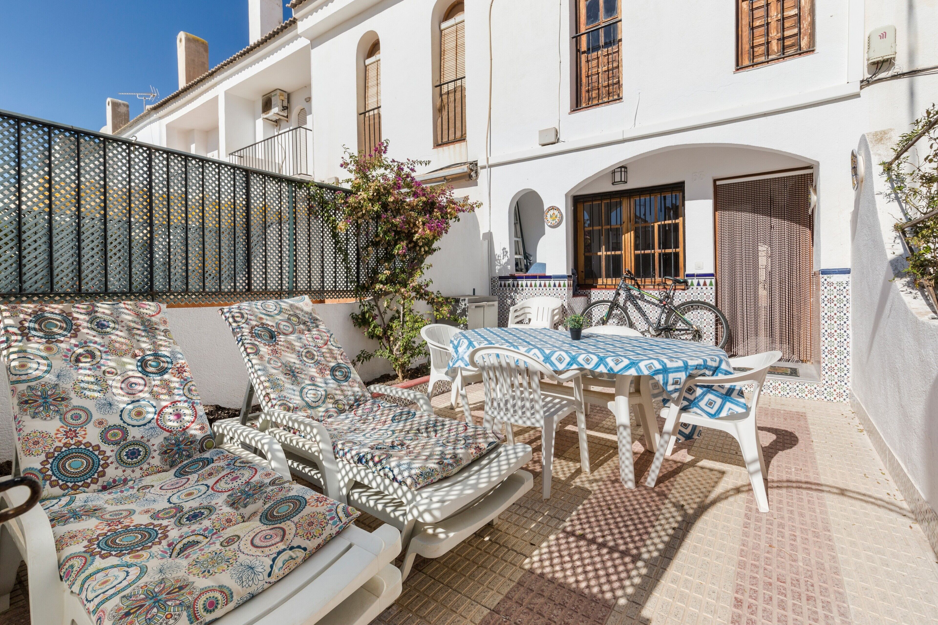 A terrace with lounge chairs, a table, and chairs, surrounded by a white building with windows and a door.