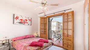 Un dormitorio con cama, ventilador de techo, puerta de madera y balcón con sillas.