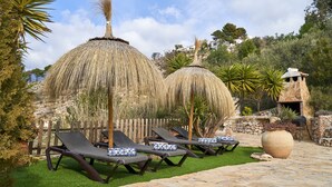 Eine Terrasse mit Lounge-Möbeln und Strohdächern, eine Steinmauer und ein großer Blumentopf.