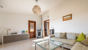 Una sala de estar con una mesa de centro de vidrio, un sofá color crema y un mueble con objetos decorativos.