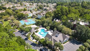 Vue aérienne d’un quartier résidentiel avec une piscine, des courts de tennis et un parking.