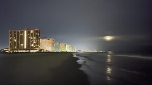 Une vue nocturne d’une ville côtière, avec des bâtiments illuminés le long de la promenade.