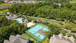 Vue aérienne d’un quartier résidentiel avec un court de tennis, une piscine et des espaces verts environnants.