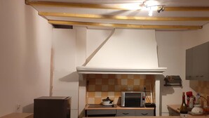 Uma cozinha compacta com micro-ondas, fogão pequeno e uma garrafa de vinho sobre o balcão.