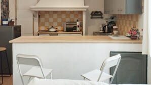 Cozinha compacta com ilha central, cadeiras brancas e micro-ondas.