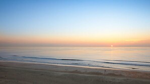 A beach at sunrise with calm waters and a clear sky.