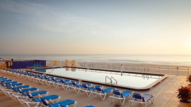 A pool area with a view of the beach, lounge chairs, and a lifeguard stand.