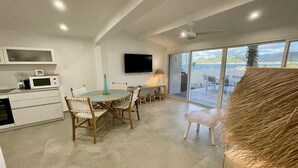 A modern kitchen with white cabinets, a dining area with wooden chairs, a flat-screen TV, and a large sliding glass door leading to a balcony with a view of the sea. - Beach front fabulous new all renovated unit 3 bedrooms 3 Baths, pools see view (Collectivité de Saint-Martin)