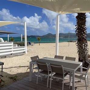Une terrasse au bord de la plage, avec une table et des chaises, une clôture blanche et un palmier.