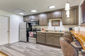 A kitchen with a refrigerator, microwave, oven, and a bar area with stools. - Riverfront Apopka Studio Near Wekiwa Springs! (Apopka)