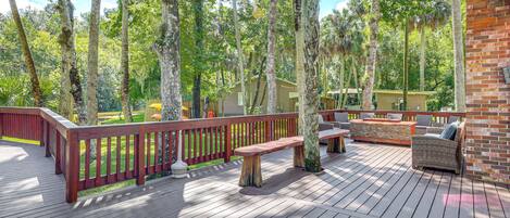An outdoor deck with wooden railings, a seating area with a bench and a table, surrounded by trees.