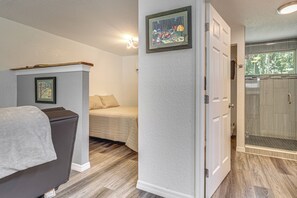 A room with a bed, a chair, a door leading to a shower area, and a framed picture on the wall. - Riverfront Apopka Studio Near Wekiwa Springs! (Apopka)