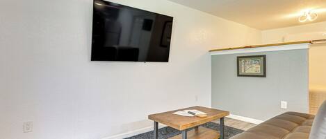 Un salon avec un téléviseur à écran plat fixé au mur, une petite table en bois, un canapé en cuir marron et un tableau encadré accroché au mur.