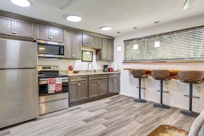Una cocina moderna con electrodomésticos de acero inoxidable, armarios de madera y una barra con taburetes.