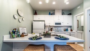 A modern kitchen with white cabinets, a central island with stools, a refrigerator, microwave, and a sink.