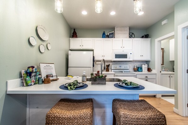 A modern kitchen with white cabinets, a central island with stools, a refrigerator, microwave, and a sink.
