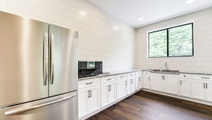 A modern kitchen with white cabinetry, stainless steel appliances, and a large window providing natural light. - Harbor Cove Condo | Ski • Beach • Explore (Harbor Springs)
