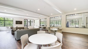 A spacious, modern room with a large round table and white chairs, a grey sofa, and a TV mounted on the wall. - Harbor Cove Condo | Ski • Beach • Explore (Harbor Springs)