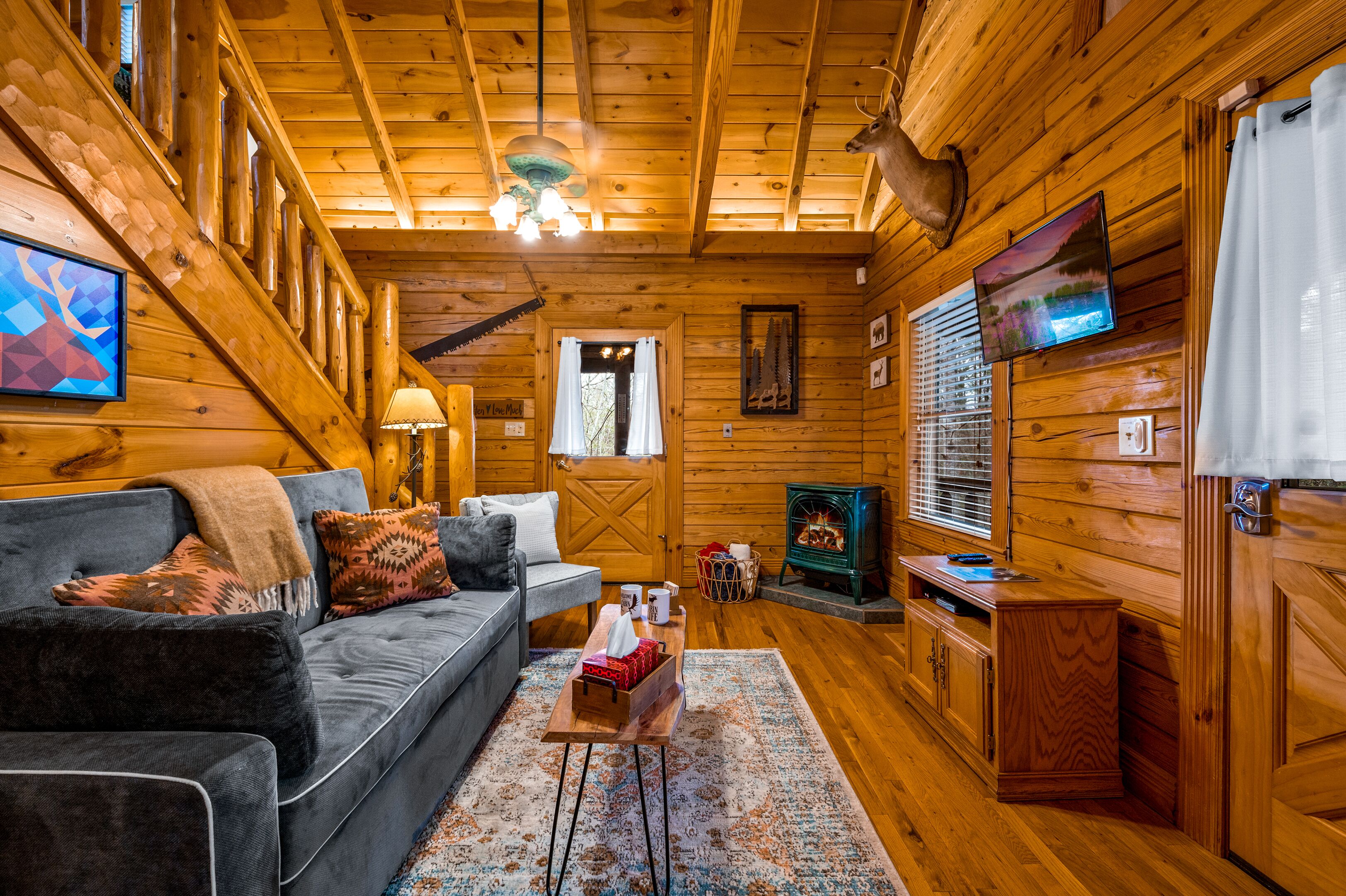 A cozy cabin interior with a sofa, a fireplace, a television, and wooden walls.