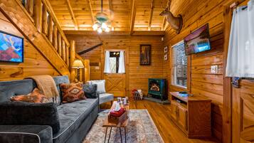 Un acogedor interior de cabaña con sofá, chimenea, televisor y paredes de madera.