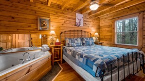 A wooden cabin bedroom with a large bed, a wooden bathtub, and a window with blinds. - *Starlink Wifi* Peaceful Log Cabin Near National Park & Dollywood (Sevierville)