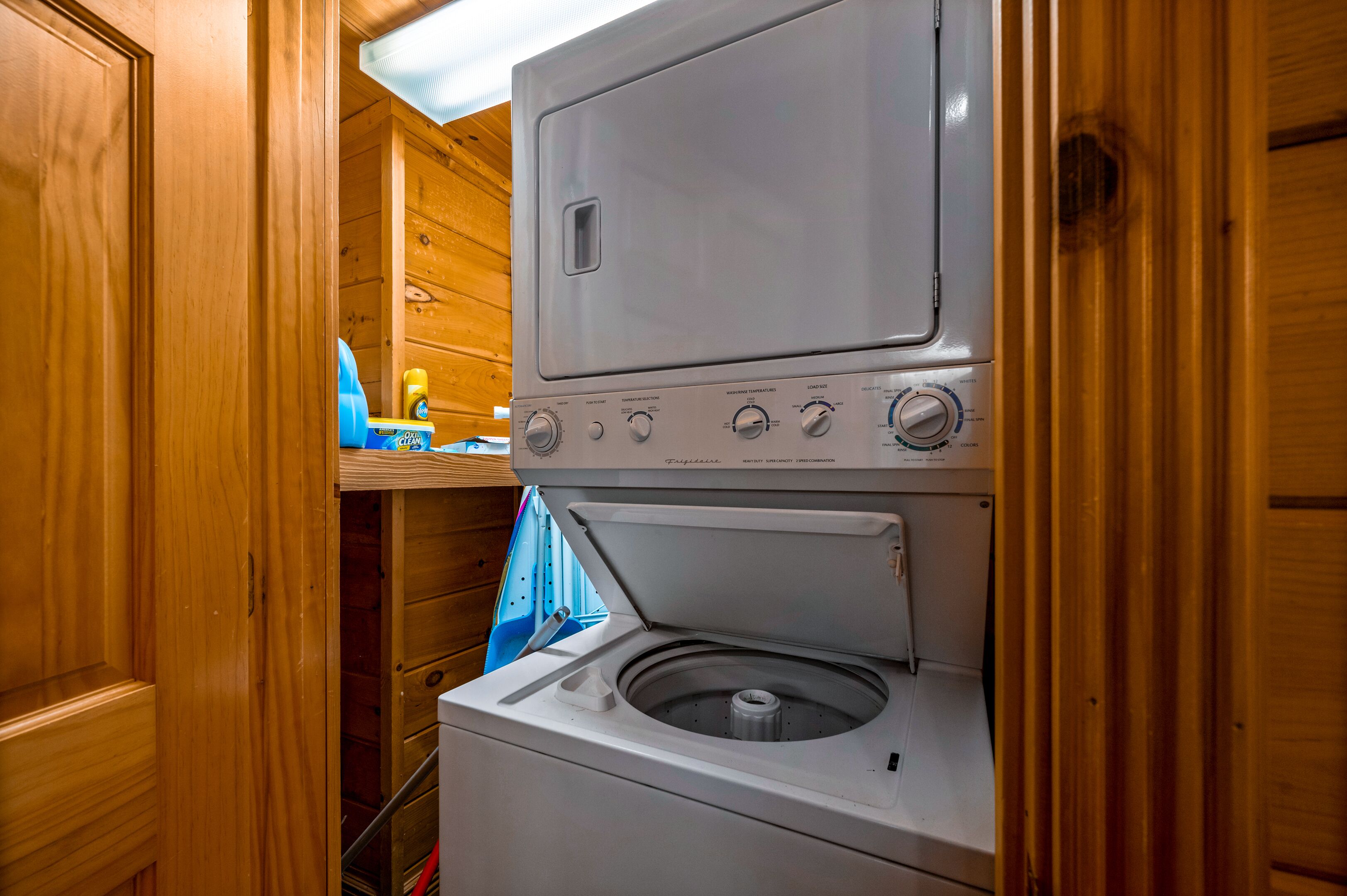 A compact laundry area with a front-loading washer and dryer, wooden walls, and a blue towel rack.