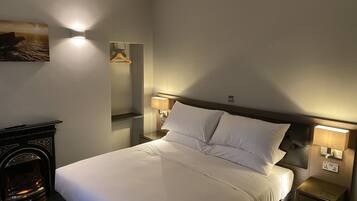 A hotel room with a neatly made bed, bedside lamps, a small table, and a fireplace.